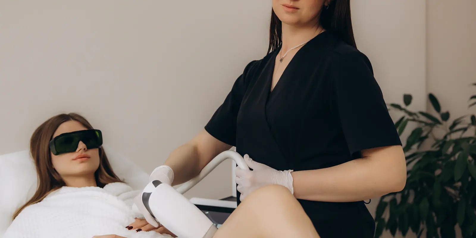 A practitioner in protective goggles performing a laser treatment on a patient’s leg in a clinic room.