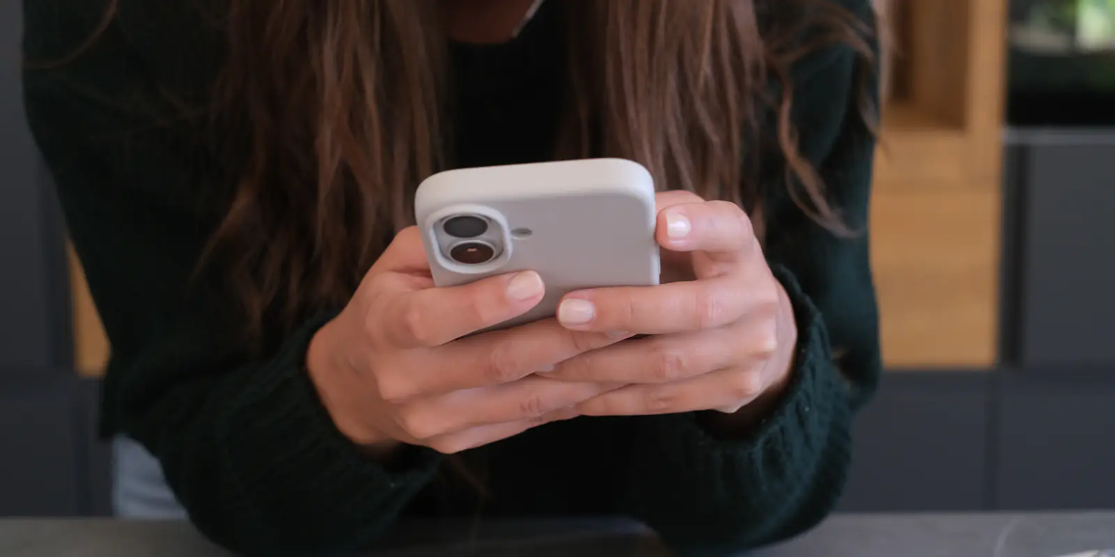 Close-up of a person’s hands typing on a smartphone at a stone counter in a warm interior.